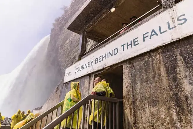Tourists in yellow rain ponchos experiencing the waterfall mist
